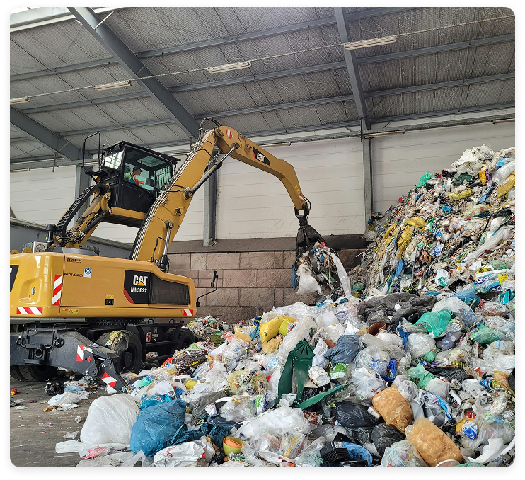 Ein Bagger sortiert große Mengen an Müll und Plastikabfällen in einer Recyclinghalle.