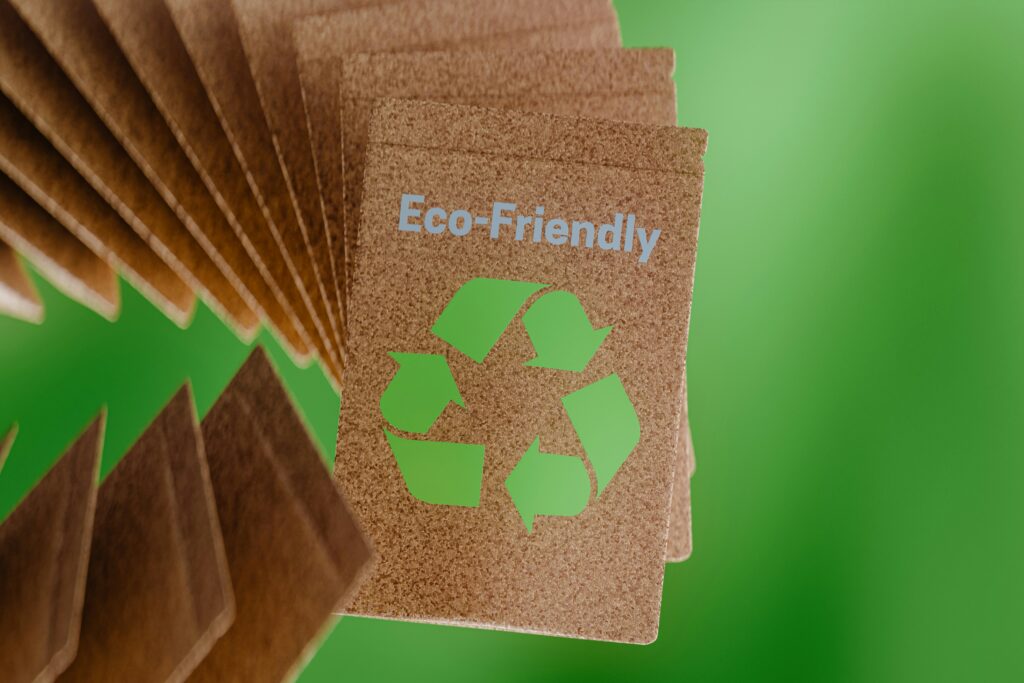 Karten aus braunem Karton mit grünem Recycling-Symbol und der Aufschrift „Eco-Friendly“ vor einem grünen Hintergrund.