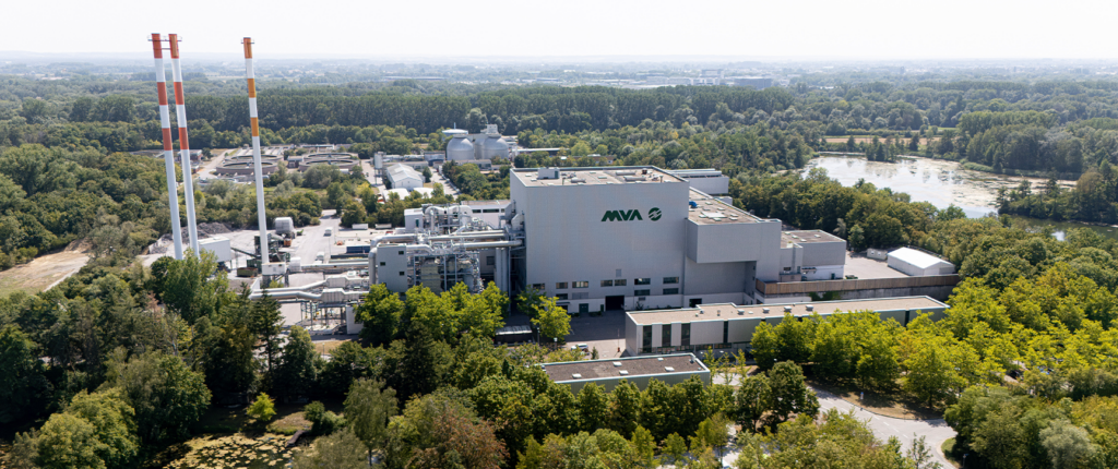 Großes Industriegebäude von AVA inmitten einer grünen, bewaldeten Umgebung, aufgenommen aus der Vogelperspektive an einem sonnigen Tag.