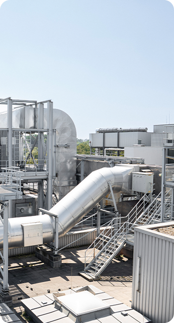 Industrieanlage mit großen Metallrohren, Klimaanlagen und verschiedenen technischen Strukturen im Freien bei Tageslicht.